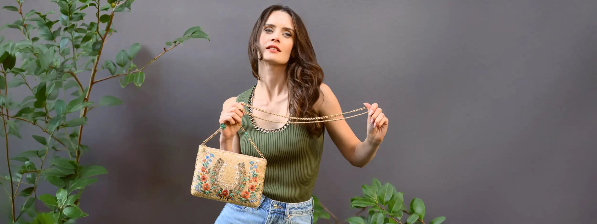A beige embroidered handbag with a floral and horseshoe design, featuring gold-toned chain straps.