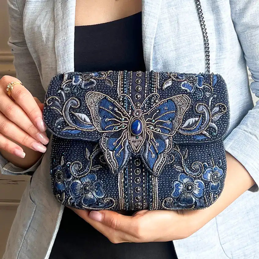 A dark blue beaded clutch bag with an ornate butterfly and floral embroidery.