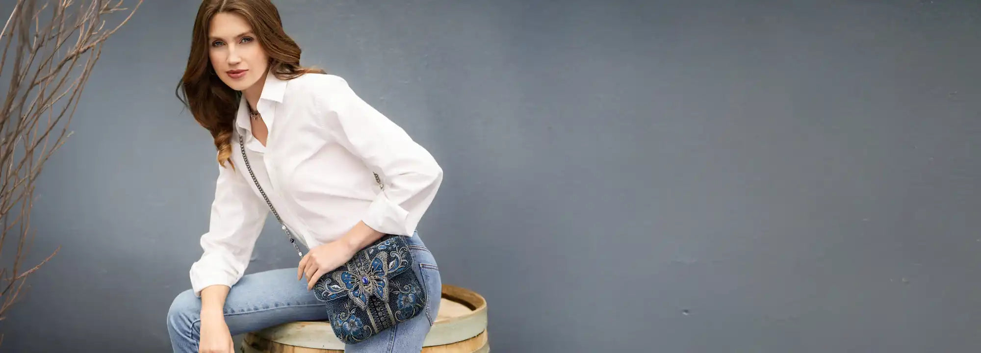 A stylish woman modeling a white button-up shirt, blue jeans, and a patterned crossbody bag.