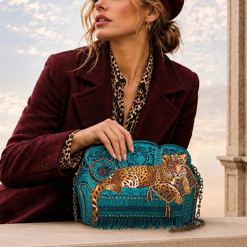 Teal beaded clutch featuring an embroidered leopard lounging on a cushion, accented with fringe and chain strap.
