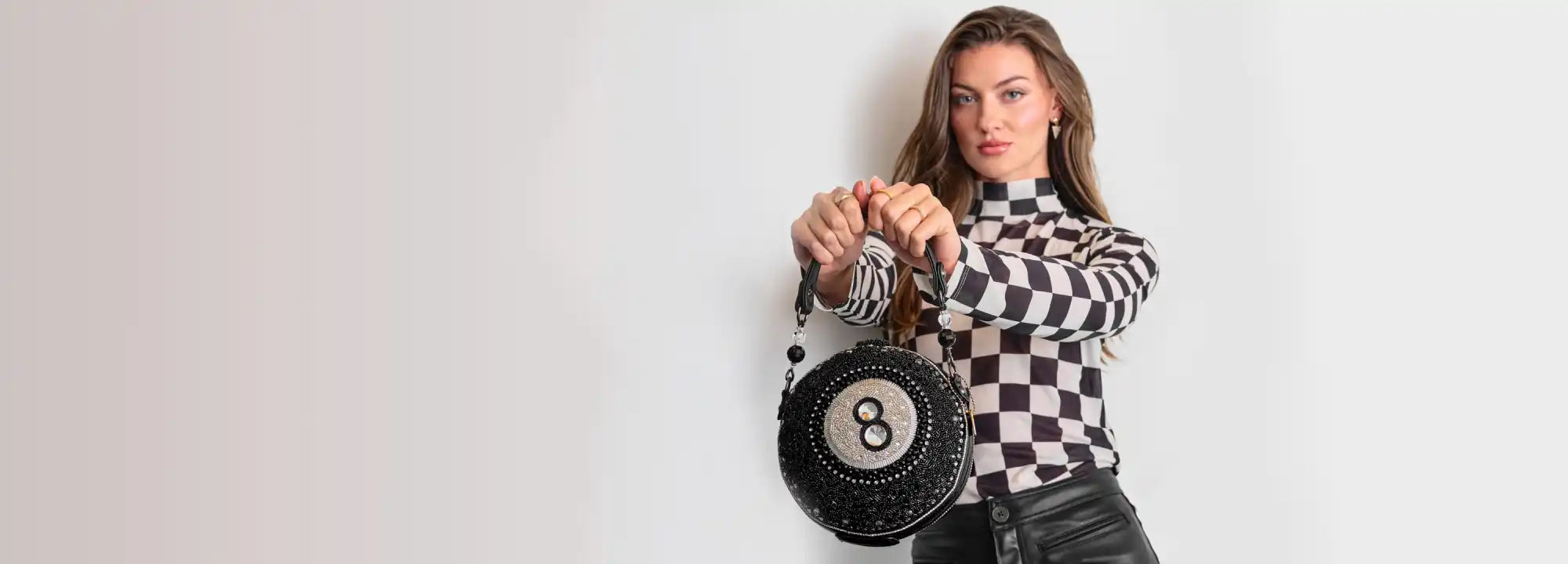 A woman wearing a black and white checkered top and a black skirt, holding a round black purse with an ’8’’ on it.
