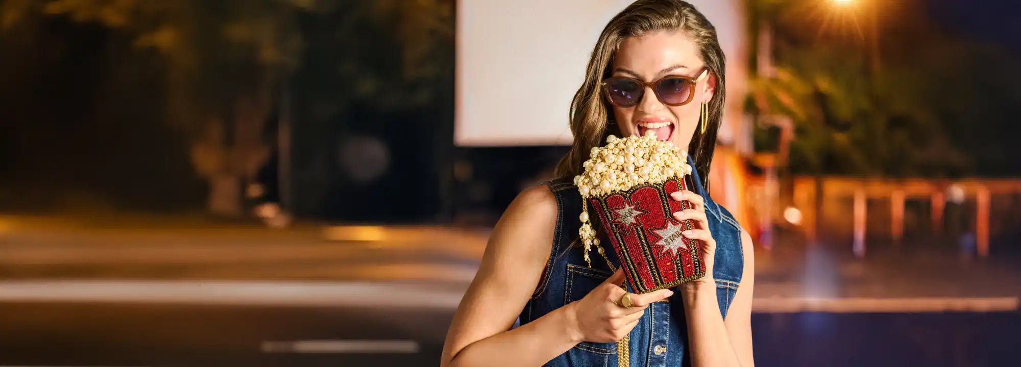 A woman in sunglasses holding a decorative container overflowing with popcorn.